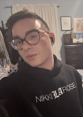 Person wearing a black hoodie with 'Nikki La Rose' branding, standing in a room with furniture and decor.